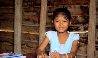 Em Siu H’Han ngồi học bài trong căn nhà sàn cũ nát