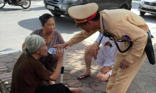 Cụ già được chiến sĩ CSGT dìu vào gốc cây sau khi bị say nắng trên đường.