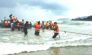 Lực lượng cứu hộ vật lộn sóng lớn nguy hiểm đưa ngư dân và chiếc thuyền chìm vào bờ an toàn (ảnh Ngọc Bình)