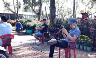 Vắng khách, người bán hoa Tết ngồi nghịch điện thoại giết thời gian.