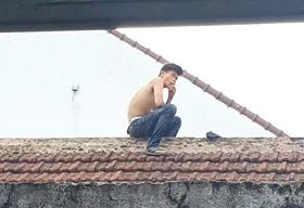 Nam thanh niên nghi ngáo đá đột nhiên leo mái nhà, liên tục la hét, dọa đâm bụng mình. Ảnh: Dân Việt