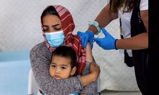 Một phụ nữ di cư bế con khi đang được tiêm phòng ở Hy Lạp ngày 3/6. (Ảnh: Reuters)