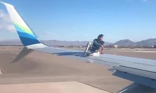 Người đàn ông chưa rõ danh tính ngồi vắt vẻo trên cánh chiếc máy bay chuẩn bị cất cánh. 