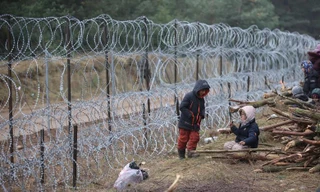 Trẻ em ngồi chơi cạnh hàng rào ngăn cách giữa Belarus và Ba Lan. Ảnh: Reuters