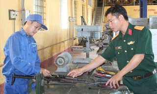 Thiếu tá Quang (bên trái) đang sửa chữa súng tiểu liên AK tại đơn vị.