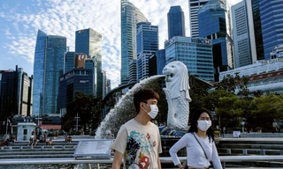 Hai thanh niên đeo khẩu trang đi ngang tượng ngư sư ở Singapore. Ảnh: AP.