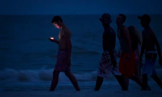 Một người trẻ nhìn vào màn hình điện thoại di động của mình khi đi dạo dọc bãi biển Ft Myers ở bang Florida, Mỹ lúc chạng vạng. Ảnh: Reuters.