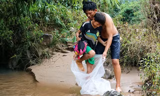 Học sinh Na Sang phải chui qua túi nilon nhờ người lớn đưa qua suối. Ảnh: VOV. 