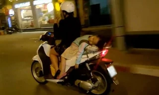 Em bé không được đội mũ bảo hiểm, nằm ngủ gật trên xe của mẹ.