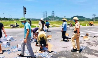 Xe container bị lật, chiến sĩ CSGT giúp thu gom hàng trăm thùng nước đổ giữa đường