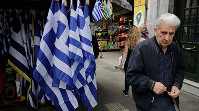 Người đàn ông đi qua một ki ốt bán cờ tại Athens. Ảnh: MB