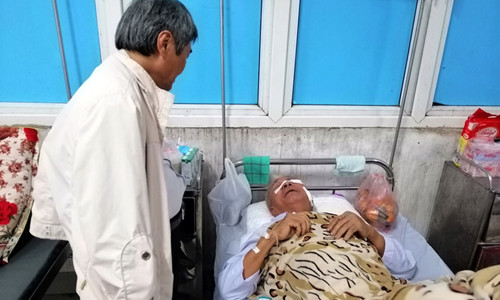 Ông Được nằm trên giường bệnh, đầu và tay chi chít vết băng bó. Ảnh: Hoàng Lam.