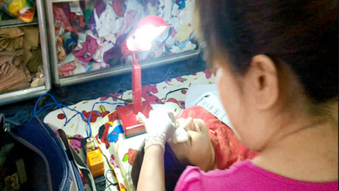 Một phụ nữ đang gây mê để xăm chân mày cho khách trong một tiệm cắt tóc. Ảnh: Thi Ngoan.
