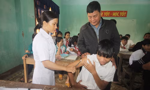 Thầy Nguyễn Khắc Điệp động viên học sinh tiêm văcxin bệnh bạch hầu. Ảnh: Đắc Thành.