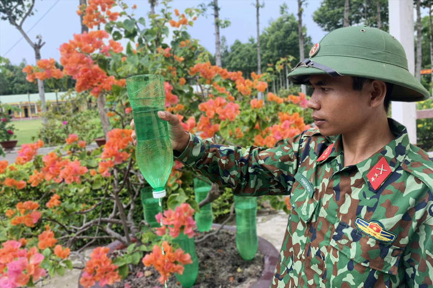 Binh nhất Thạch Mích và mô hình “Tưới nhỏ giọt bằng chai nhựa” chăm sóc các bồn hoa, cây cảnhẢnh: PV 