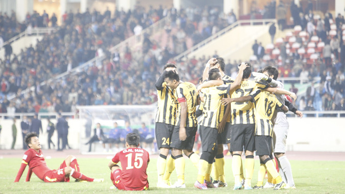 Các cầu thủ VN đổ gục xuống sân sau trận thua trong lúc ĐT Malaysia ăn mừng chiến thắng không ngờ. Ảnh: Như Ý