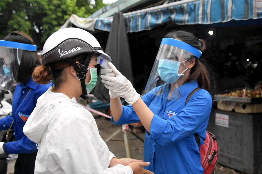 TNV kiểm tra thân nhiệt người dân tại một chốt chặn ở cổng chợ. Ảnh: Giang Thanh