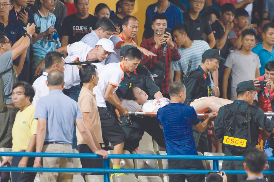 Nữ cổ động viên được đưa lên cáng đi cấp cứu sau khi bị trúng pháo sáng vào đùiảnh: VSI