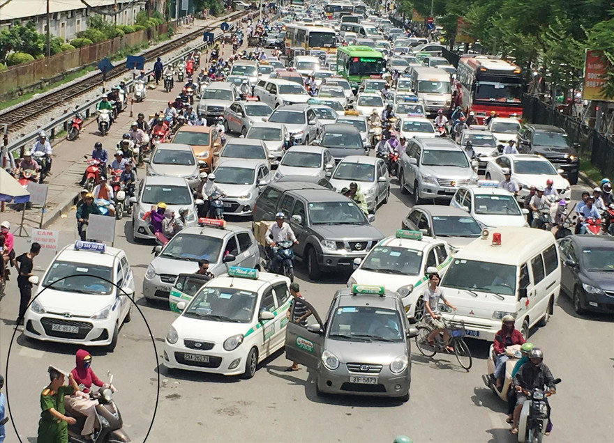 Đường Giải Phóng trước BV Bạch Mai ùn tắc nhưng taxi vẫn dàn hàng đứng đón, trả khách, còn công an có mặt (khoanh tròn) lấy báo che đầu Ảnh: A.Trọng