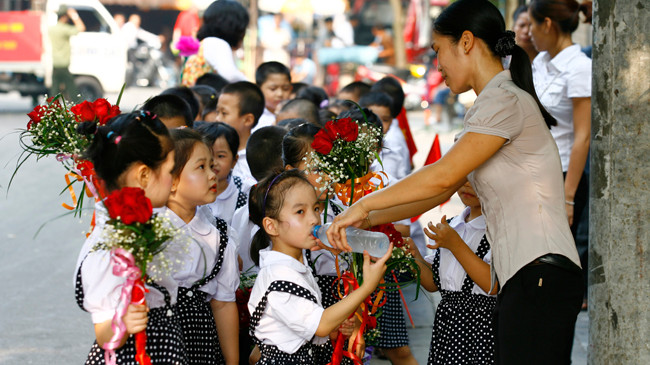 Phụ huynh phục vụ nước cho con uống vì phải đợi xếp hàng chờ khai giảng năm học 2014-2015 ở Hà Nội. Ảnh: Hồng Vĩnh.