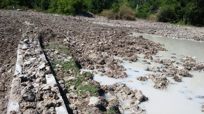 Bờ thành bằng bê tông của mương thủy lợi bị xe ủi xé nát, nằm vùi lấp trong bùn đất.