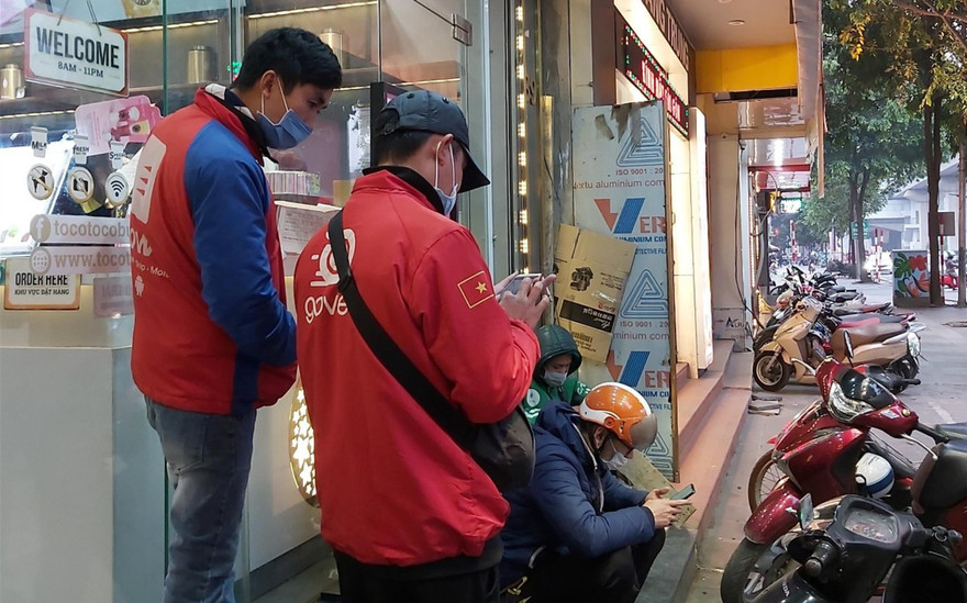 Các shipper của Grab và GoViet đang xếp hàng nhận đơn từ một cửa hàng đồ uống trên đường Quang Trung, Hà Đông, Hà Nội Ảnh: Võ Hóa 