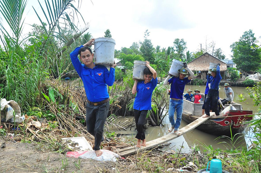 Các sinh viên tình nguyện khuân cát, đá từ dưới ghe lên bờ làm đường Ảnh: Hòa Hội