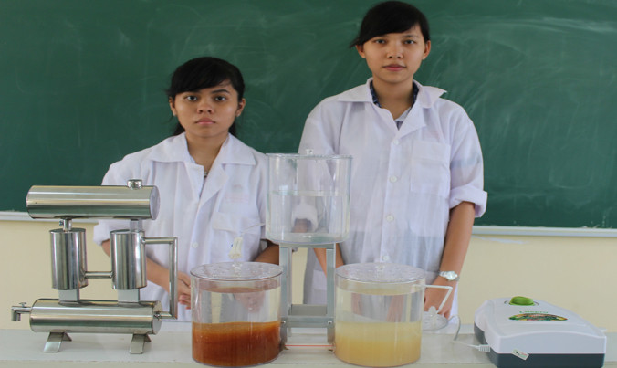 Thảo Quỳnh (bìa phải) và Hoàng Yến cạnh mô hình “Hệ thống xử lý nước mưa khép kín”. Ảnh: Xuân Lương.