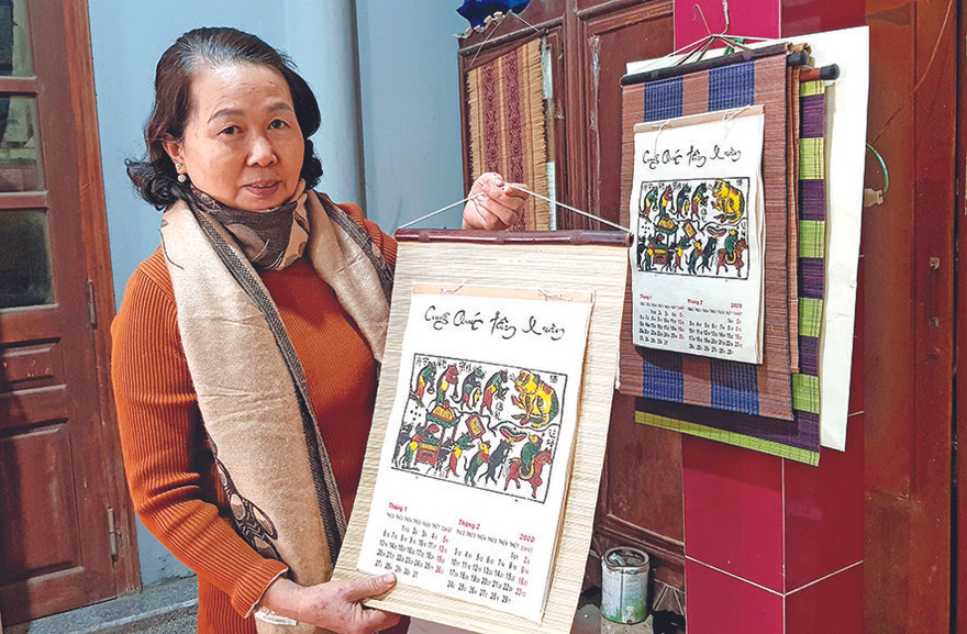 Nghệ nhân Nguyễn Thị Oanh giới thiệu cuốn lịch năm Canh Tý, với bức tranh “Đám cưới chuột” Ảnh: KIẾN NGHĨA 