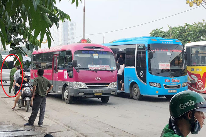 Xe khách dàn hàng ngang bắt khách trên đường nhưng một cán bộ công an (vòng tròn) làm việc tại cổng bến Giáp Bát sáng 20/8 chỉ đứng nhìn.