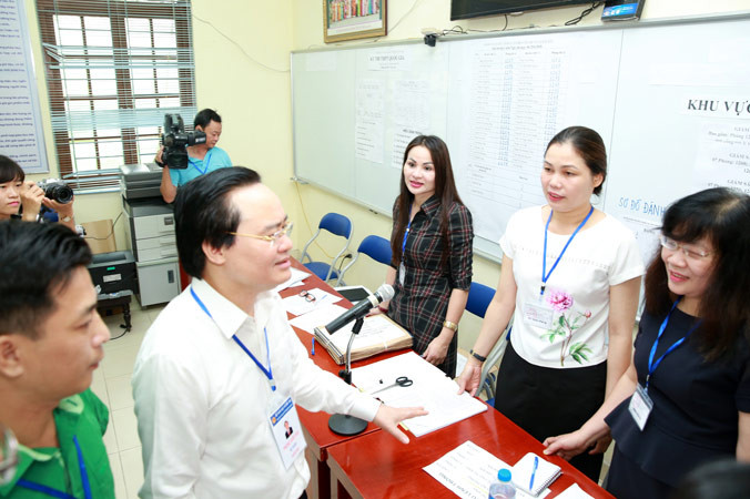 Bộ trưởng Phùng Xuân Nhạ trò chuyện với cán bộ, giáo viên làm công tác coi thi, phục vụ thi tại điểm thi THPT Yên Viên - Gia Lâm, Hà Nội. Ảnh: Như Ý. 
