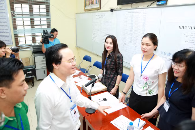 Bộ trưởng Phùng Xuân Nhạ trò chuyện với cán bộ, giáo viên làm công tác coi thi, phục vụ thi tại điểm thi THPT Yên Viên - Gia Lâm, Hà Nội. Ảnh: Như Ý. 