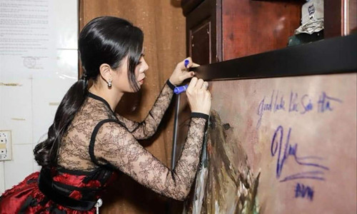 Ca sĩ Lệ Quyên đang để lại thủ bút trên tranh của họa sĩ Hứa Thanh Bình. Ảnh: Duy Anh