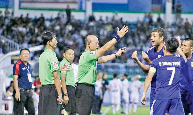 Trợ lý Phan Việt Thái (trái) và trọng tài Hoàng Anh Tuấn (giữa) bị cầu thủ Quảng Nam bao vây phản đối ở trận HAGL – Quảng Nam. Ảnh: Trần Khánh.