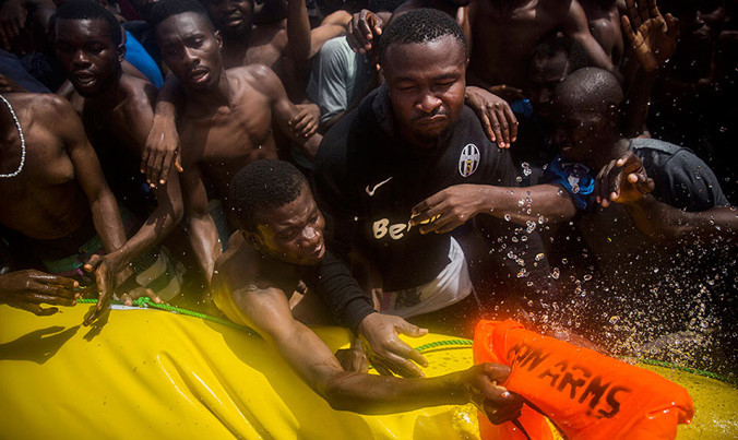 Người di cư trên chiếc thuyền nhỏ với tay lấy áo phao. Ảnh: AP.