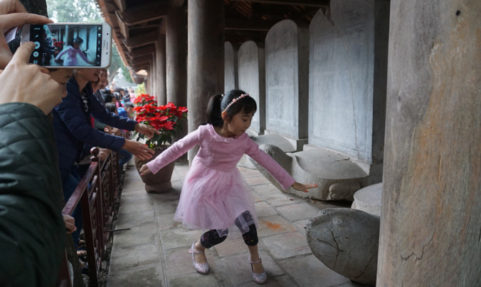 Một số phụ huynh vẫn xui con trẻ vượt rào vào sờ đầu rùa ở Văn Miếu. Ảnh: Nguyên Khánh.