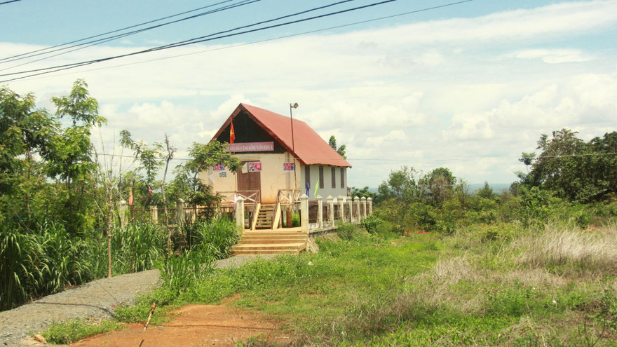 Nhà cộng đồng trơ trọi giữa bãi đất trống cỏ mọc um tùm 