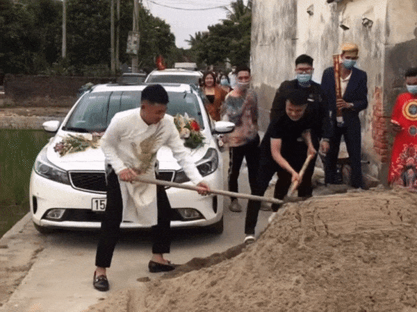 Chú rể cùng một số thanh niên nhà trai phải xúc cát để dọn đường xe qua. Ảnh cắt từ clip/Đức Thiện. chu re xuc cat tren duong don dau anh 1