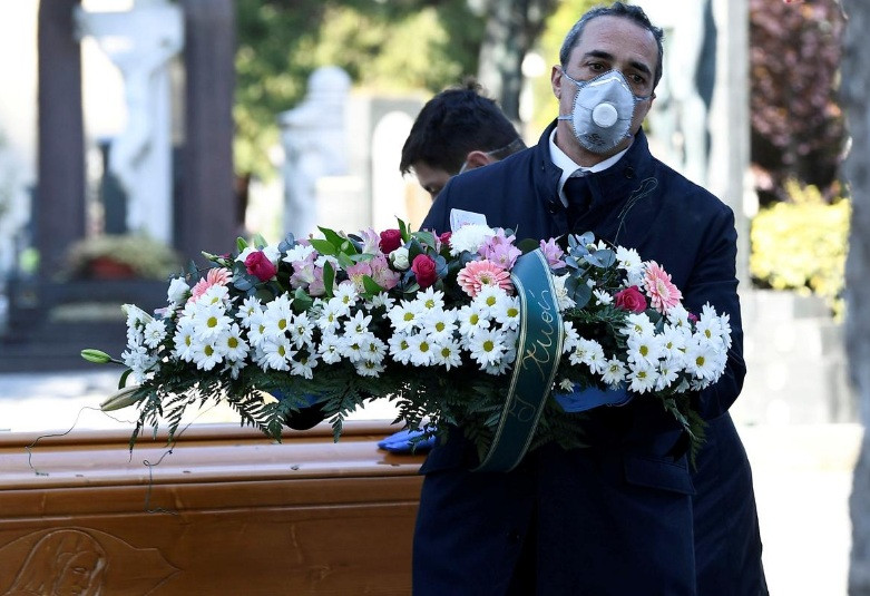 Một nhân viên tang lễ Italy đeo khẩu trang trong đám tang của bệnh nhân Covid-19. (Ảnh: Reuters)