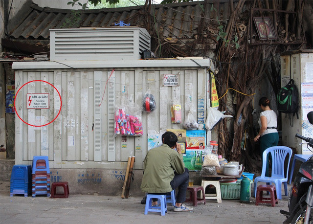 Mặc dù có biển cảnh báo nguy hiểm, không được lại gần ( ở vòng tròn đỏ) tại bốt điện này, nhưng người bán hàng nước và vị khách này vẫn ngồi sát. Ảnh chụp tại vỉa hè phố Vũ Tông Phan