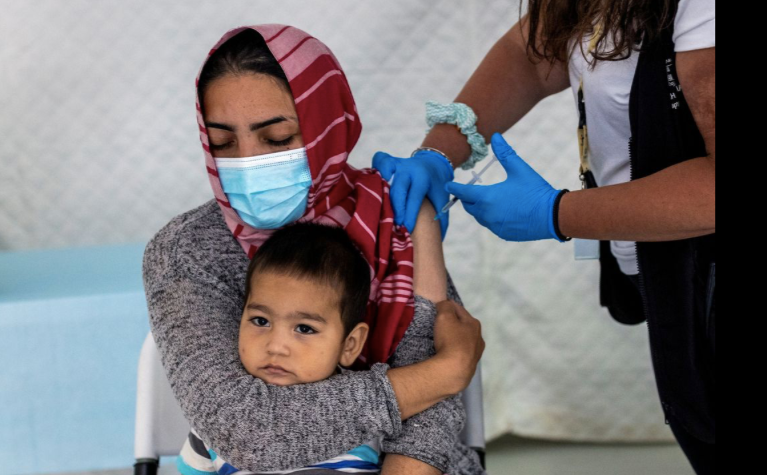 Một phụ nữ di cư bế con khi đang được tiêm phòng ở Hy Lạp ngày 3/6. (Ảnh: Reuters)