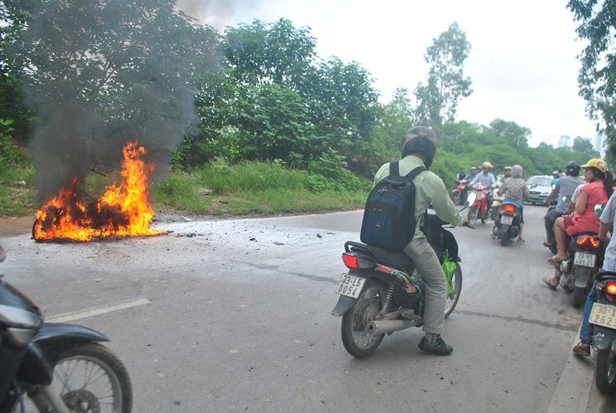 Nhiều người đi đường bất lực nhìn chiếc xe bị thiêu rụi do không có đồ chữa cháy. Ảnh: Lương Bằng.