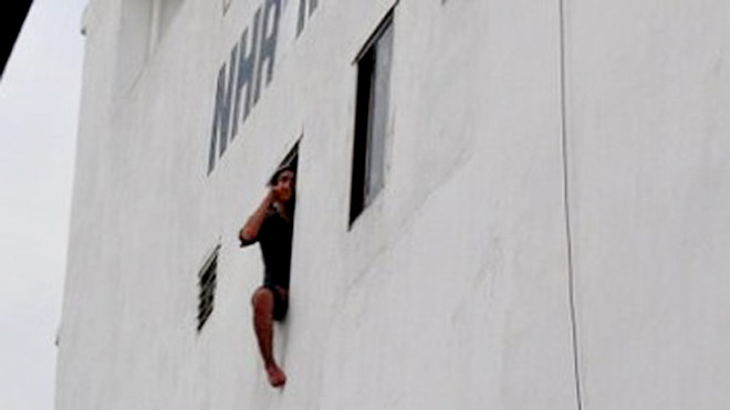 Đối tượng Võ Đinh Thế Long thò chân ra cửa sổ đòi nhảy lầu tự tử. Ảnh: HC