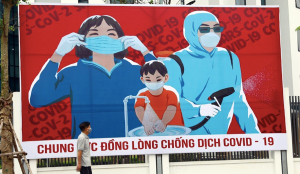 Một người đàn ông đi qua tấm áp phích kêu gọi người dân đoàn kết chống COVID-19. (Ảnh: Xinhua)