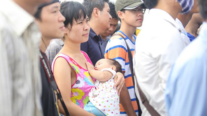 Cổ động viên này vừa bế con, vừa xếp hàng chờ mua vé. Chị sẽ còn phải chờ lâu vì hàng người còn khá dài. (Ảnh: Thu Hằng/Vietnam+)