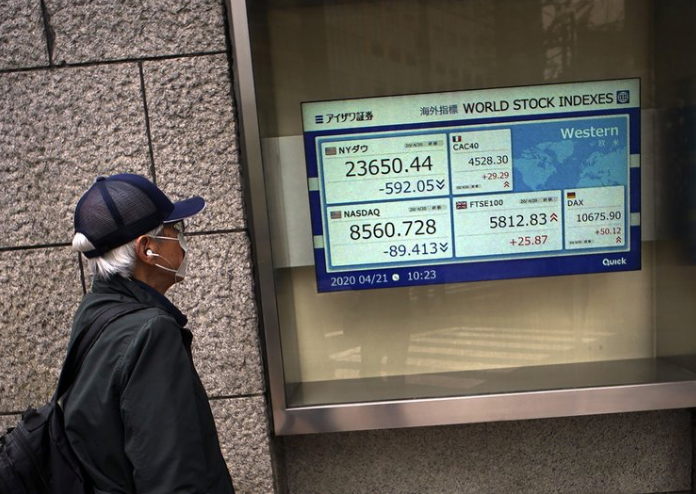 Một người đàn ông đeo khẩu trang nhìn bảng điện tử chỉ số chứng khoán thế giới bên ngoài một công ty chứng khoán ở Tokyo ngày 21/4. (Ảnh: AP)