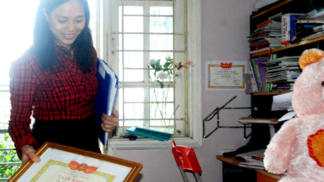 Tay phải cầm tấm bằng khen chống tiêu cực, tai trái chị "Nguyệt Hoài Đức" ôm hàng tệp những nội dung tin nhắn khủng bố, đe dọa trả thù. Phía sau tấm bằng khen chống tiêu cực