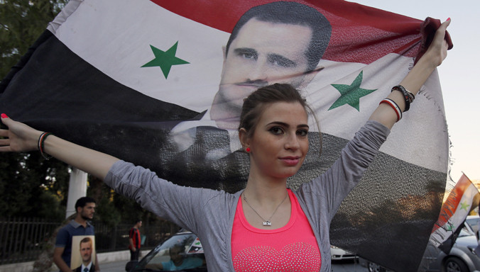 Một phụ nữ Syria mang quốc kỳ nước này có hình chân dung của Tổng thống Assad. Ảnh: AFP.