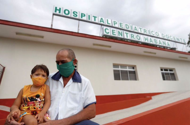 Một ông bố bế con trai bên ngoài bệnh viện ở Hanava, nơi đang triển khai tiêm vắc-xin COVID-19 cho nhóm trẻ từ 2 tuổi. (Ảnh: EPA)