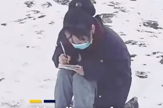 Cô nữ sinh ngồi học bài trên núi phủ đầy tuyết. (Ảnh từ clip)